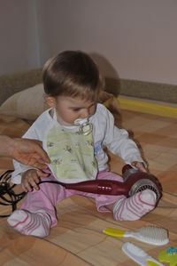 Cropped hand of mother holding boy playing with hair dryer on bed at home