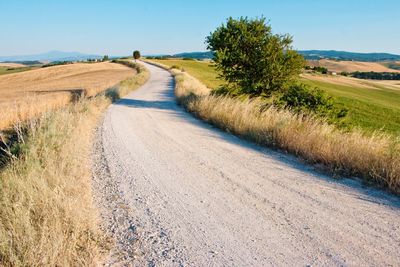 Dirt road amidst field against sky