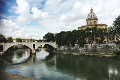 Arch bridge over river amidst buildings against sky