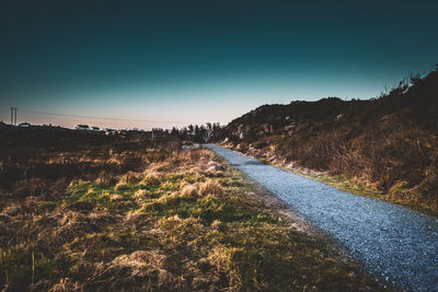 Road amidst field against clear sky