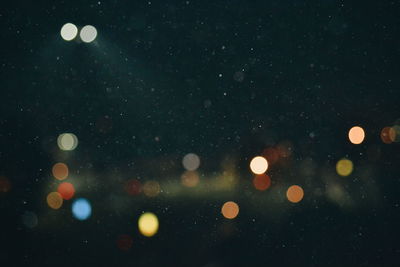 Defocused image of illuminated lights against sky at night