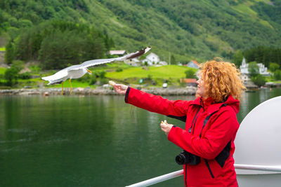 Side view of woman feeding seagull flying over lake