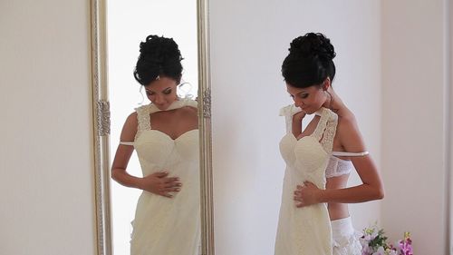 Reflection of bride trying wedding dress in fitting room on mirror