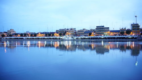 River by illuminated buildings against sky at dusk