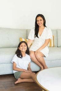 Portrait of smiling mother and daughter sitting at home