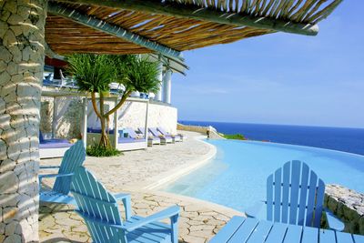 Empty chairs and lounge chair by sea against sky