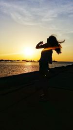 Silhouette woman standing on beach against sky during sunset