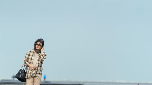 Portrait of smiling woman standing against clear sky