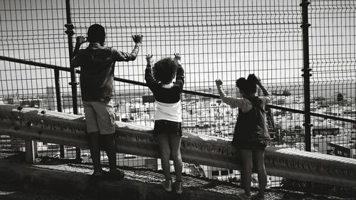 Rear view full length of siblings looking at townscape through chainlink fence