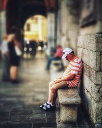 Rear view of man sitting on street against building in city