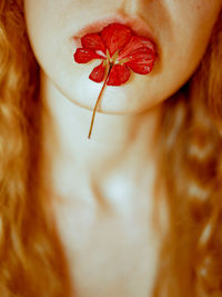 High angle view of young woman holding a red flower with her lips. blond hair, red head. 