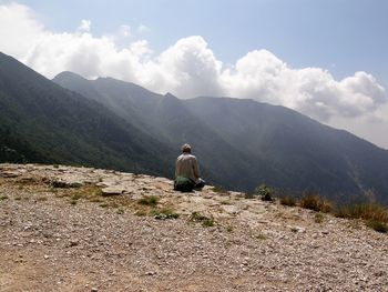 Rear view of man sitting on mountain against sky