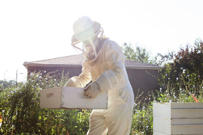 Female worker carrying beehive at farm during sunny day