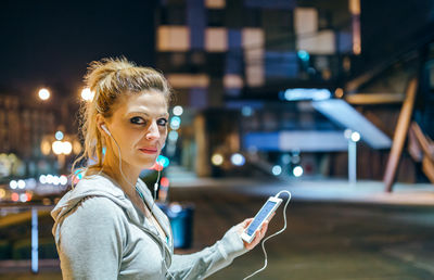 Portrait of young blonde woman looking at camera while listening music on mobile phone application
