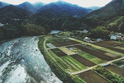 Scenic view of river by agricultural field and mountains