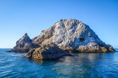 Rock formation in sea against clear blue sky