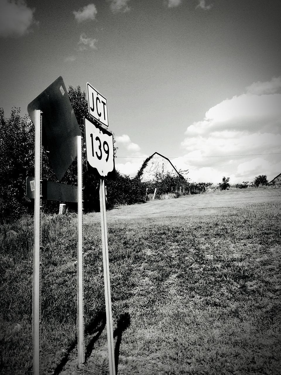 ROAD SIGN ON FIELD BY TREES AGAINST SKY