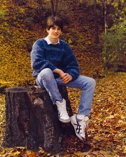 Full length portrait of teenage boy sitting on tree stump over field during autumn