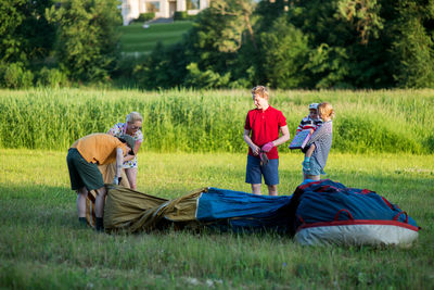 Pilot with people standing by hot air balloon on grassy field during sunset