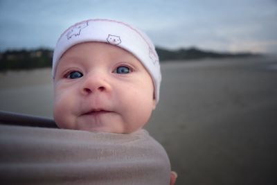 Close-up portrait of cute baby girl wrapped in fabric at beach