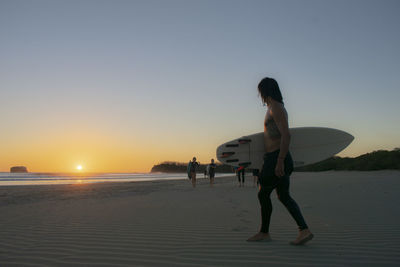 Low angle view of man with surfboard walking on beach against sky