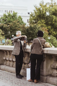 Senior man photographing woman through camera on bridge during weekend