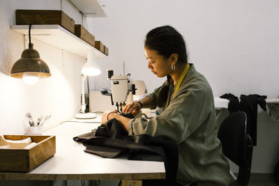 Side view of young seamstress making dress using sewing machine while working at store