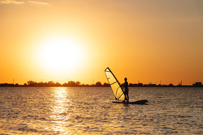 Woman windsurfer silhouette at lake sunset. beautiful beach landscape. summer water sports 