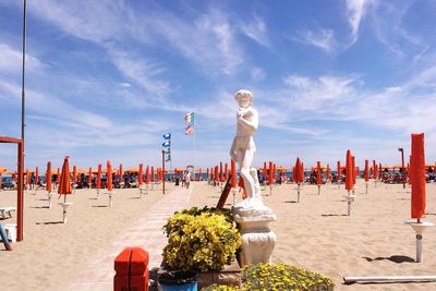 Statue and closed parasols at beach on sunny day