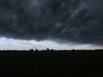 Silhouette of trees on field against storm clouds