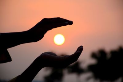 Close-up of silhouette hand against sunset sky