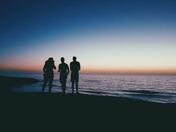 Silhouette friends standing by sea during sunset