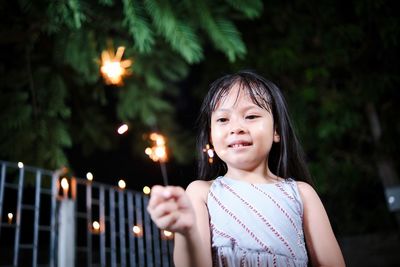 Portrait of young woman standing against illuminated christmas tree