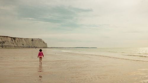Rear view of woman walking at beach against sky
