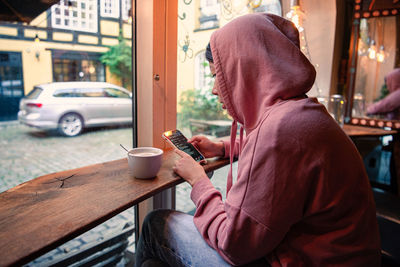 A girl looks into her smartphone and drinks a coffee sitting near the window. copenhagen, denmark