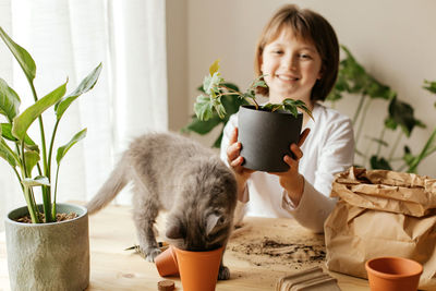 A girl with a kitten transplants home plants into a ceramic pot. curious and funny animals. 
