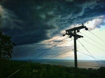 Low angle view of electricity pylon against cloudy sky