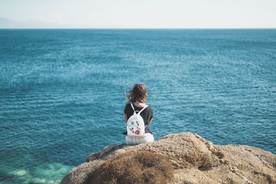 Woman sitting on rock by sea against clear sky