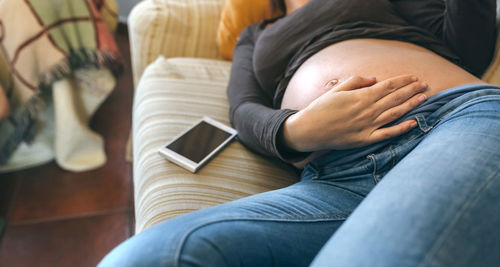 Midsection of woman touching abdomen while lying on sofa at home