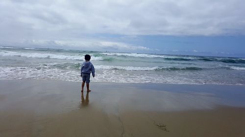 Rear view of boy standing on shore at beach