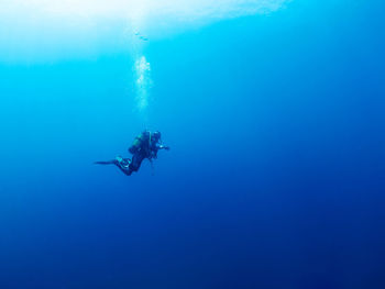 Unrecognizable professional diver in wetsuits and flippers swimming in deep blue sea with clear water