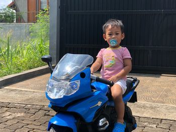 Portrait of cute boy with pacifier in mouth sitting on toy motorcycle on footpath
