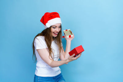 Smiling young woman holding hat while looking away against blue sky