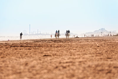 People riding horses at beach against clear sky