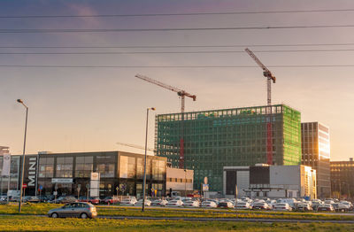 Construction site by buildings in city against sky during sunset