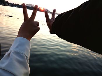 Midsection of man holding sea against sky during sunset