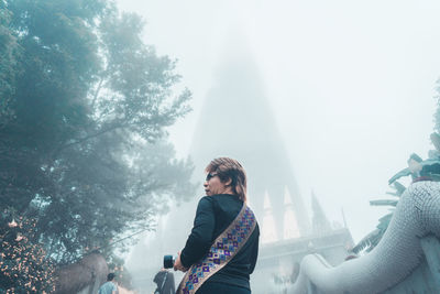 Side view of woman standing by trees against sky