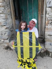 Portrait of smiling senior man with girl holding kite while sitting against door