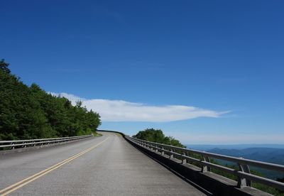 Empty road along trees against sky