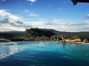 Young woman relaxing on infinity pool against sky